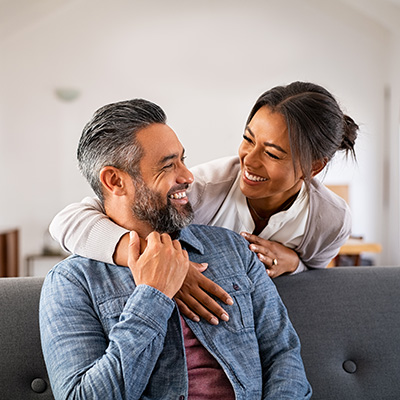 A man and woman sharing a joyful moment with smiles on their faces while embracing each other on a couch.